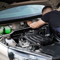 A mechanic reaching into an open car engine bay