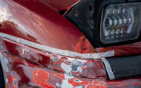 Close-up of a damaged and peeling car bumper near the headlight