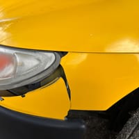 Close-up of a damaged yellow car front bumper