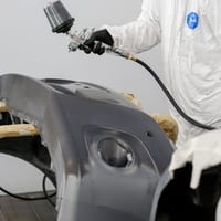 A painter in protective gear spraying a car fender