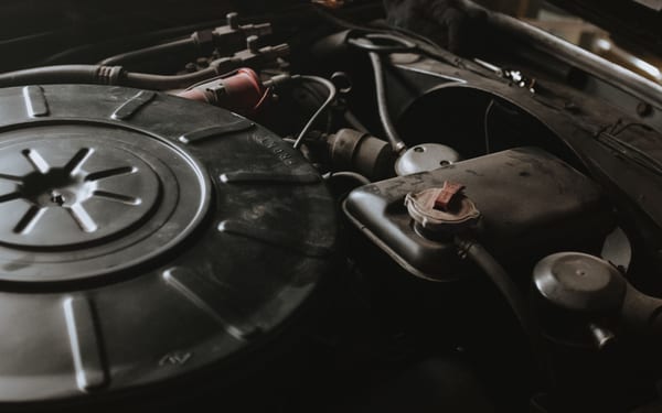 A mechanic working under an open car hood at dusk