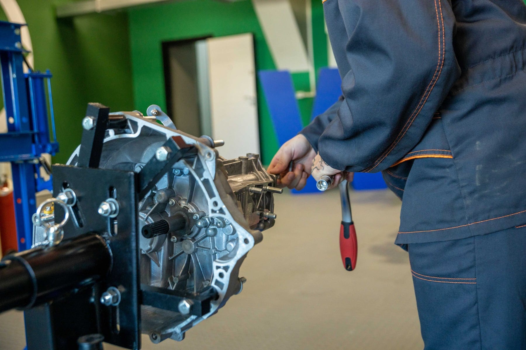 A mechanic's hands using tools on a gearbox mounted on a workshop stand