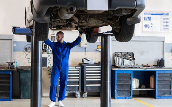A mechanic standing under a car raised on a two-post lift